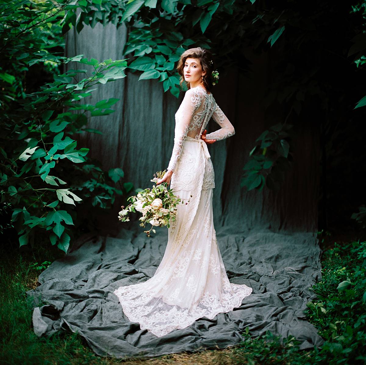 film bridal portrait with lace dress and bouquet in front of savage muslin backdrop outdoors